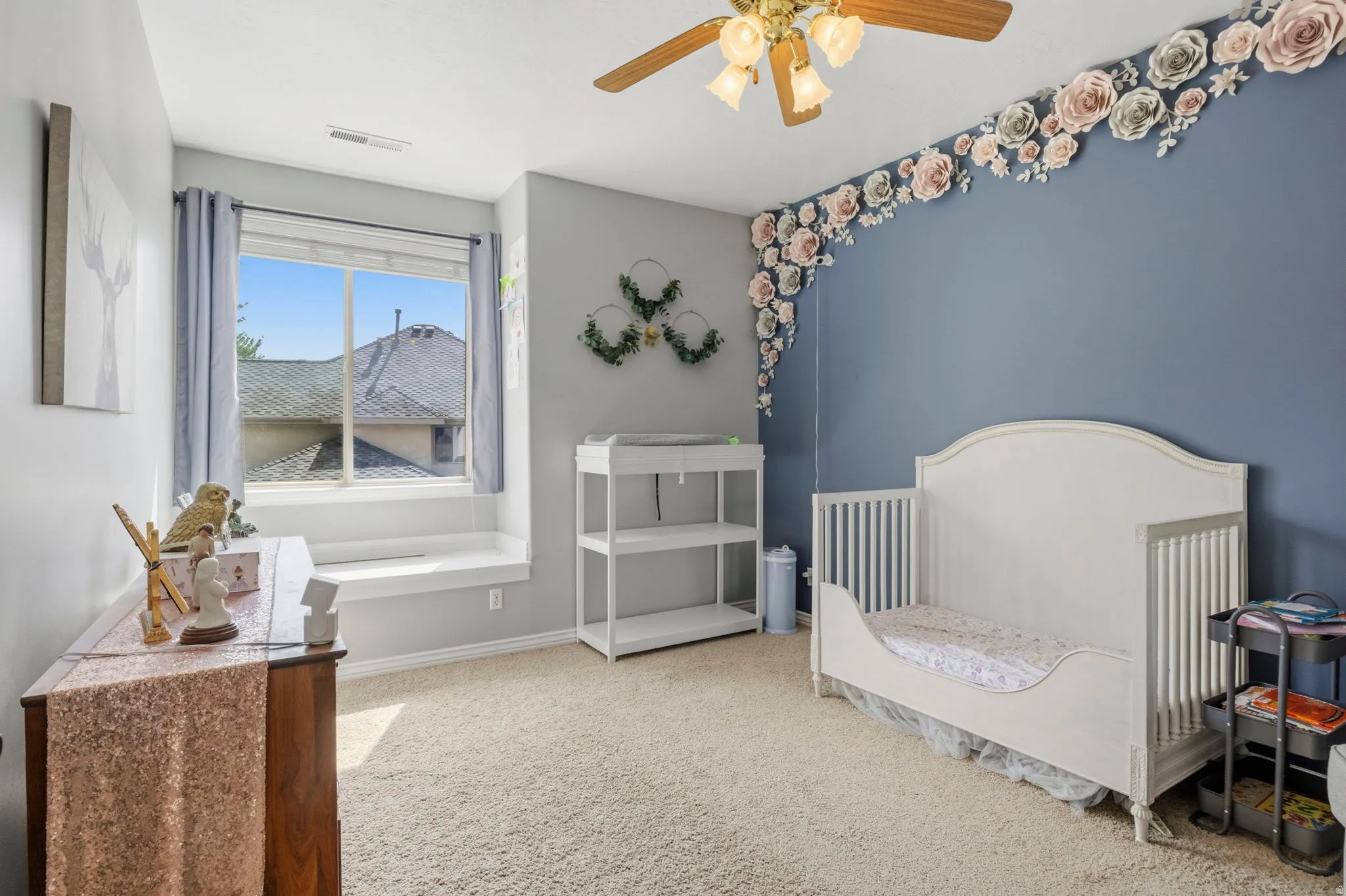 Bedroom featuring a window with integrated window seat, light-colored carpet, a ceiling fan with integrated lighting, and a painted accent wall