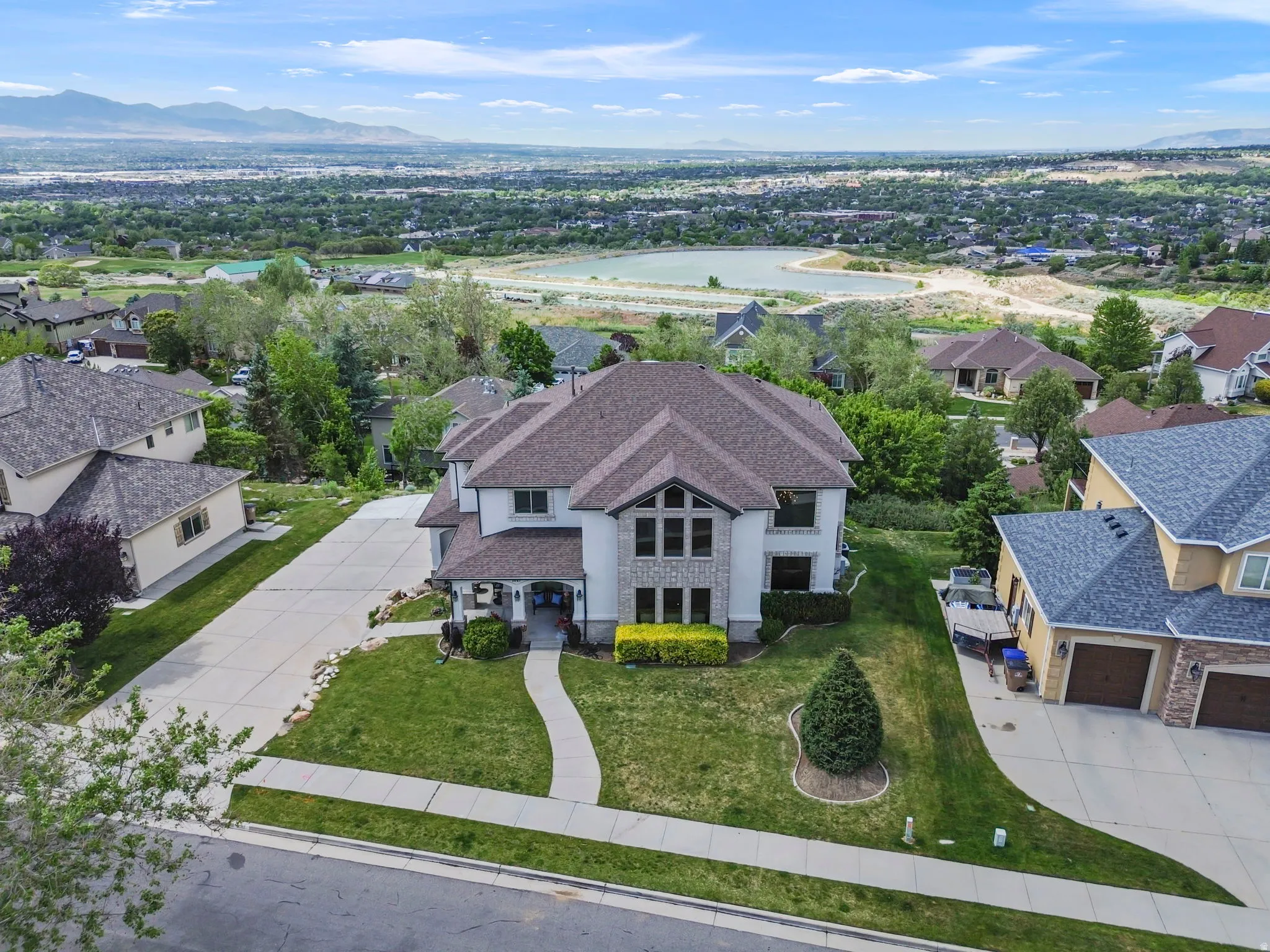Expansive property featuring a multi-level home with a tan exterior, stone accents, and a dark shingle roof