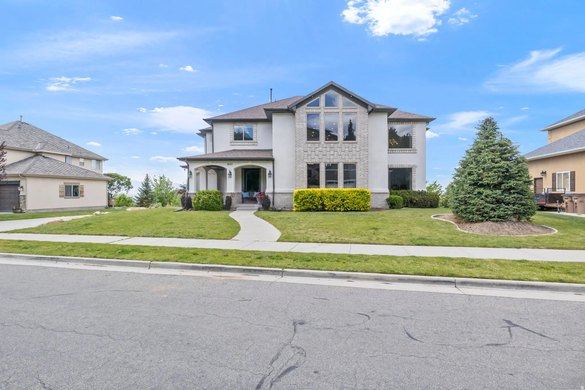 Two-story residence featuring a stucco and stone facade, arched portico entry, large bay windows, and a concrete walkway
