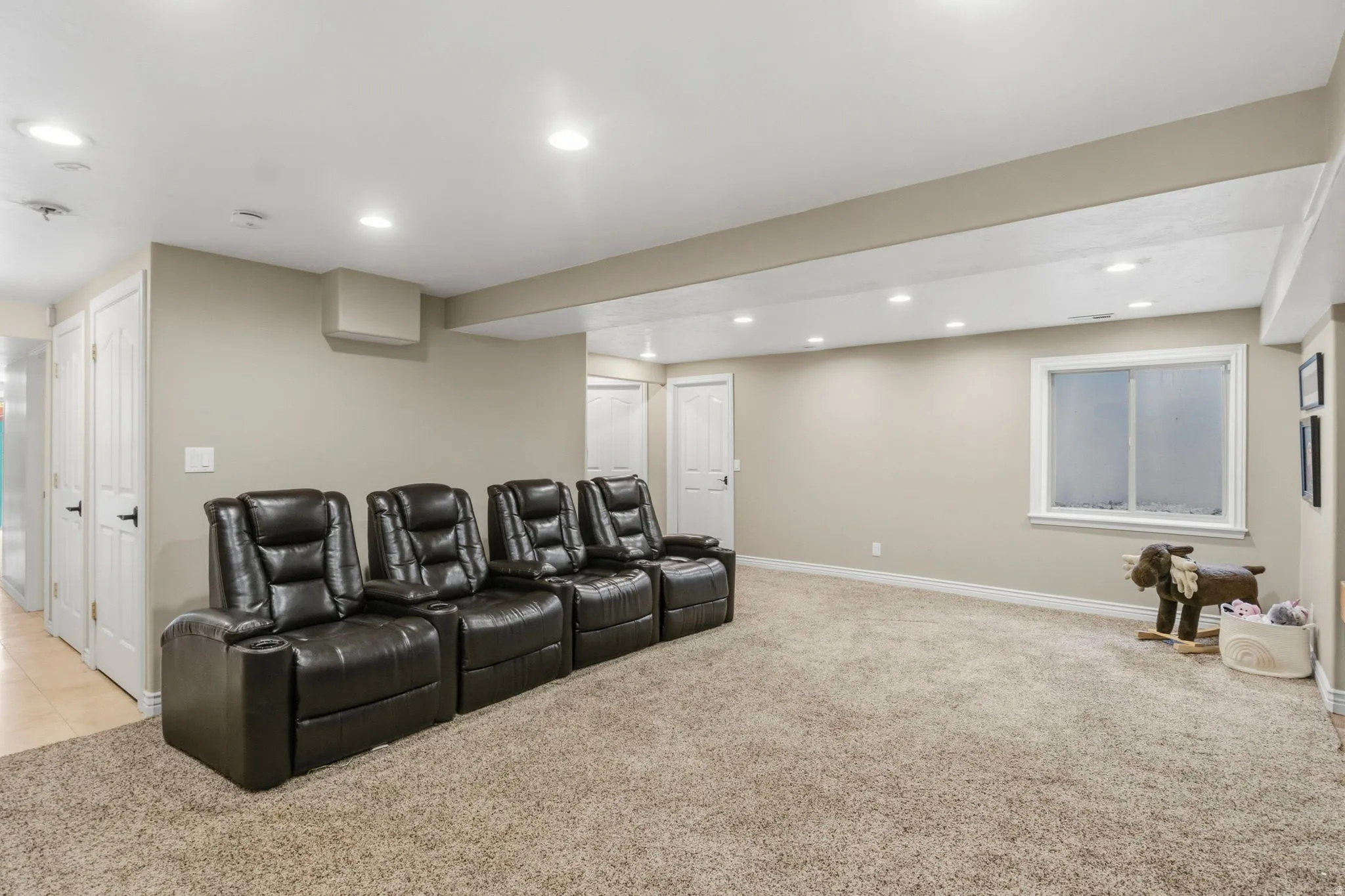 Spacious room with plush carpeting, recessed lighting, neutral wall tones, and a white-trimmed window