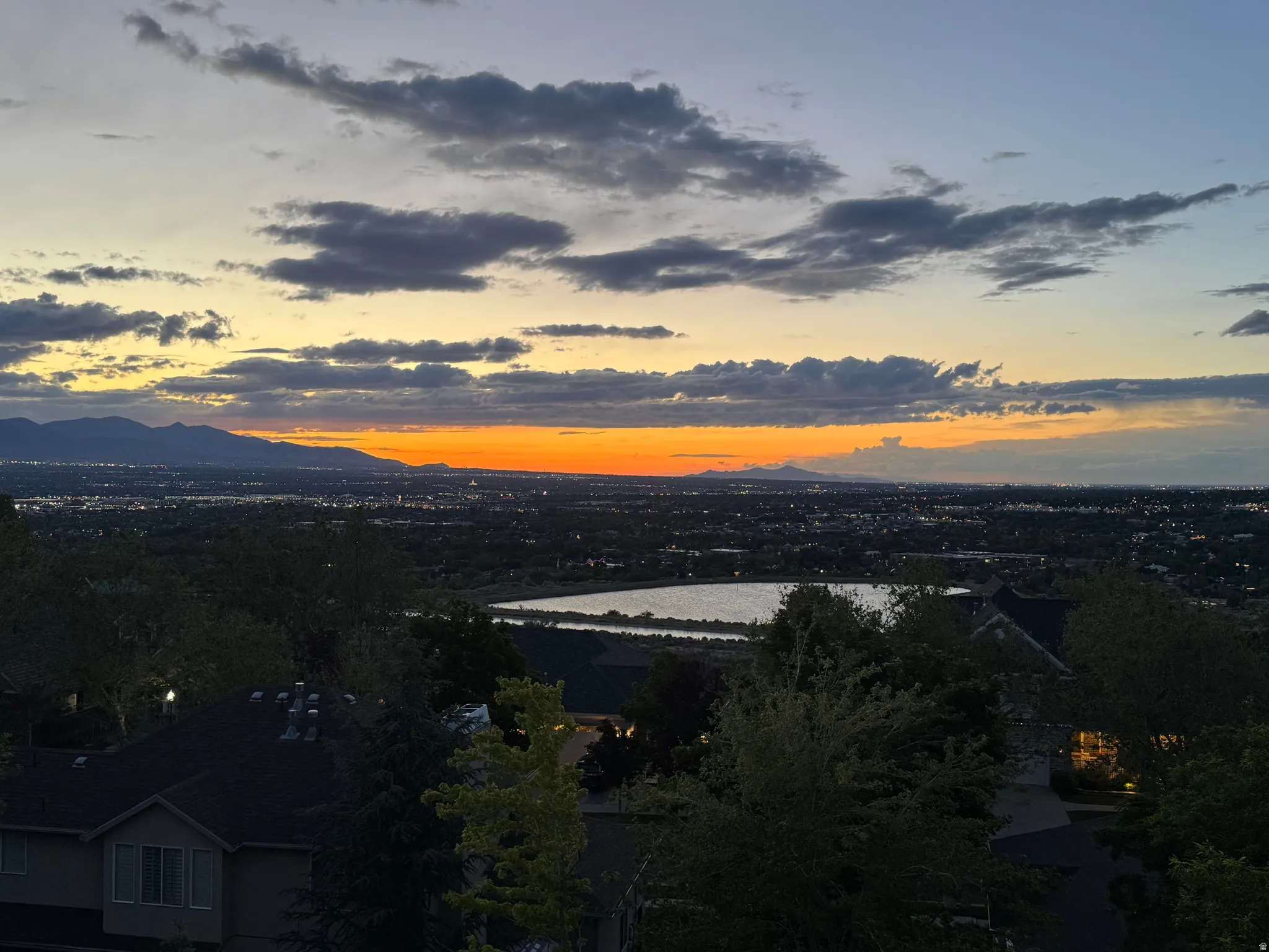 Expansive panoramic scenery featuring a body of water, distant city lights, and a mountain range backdrop
