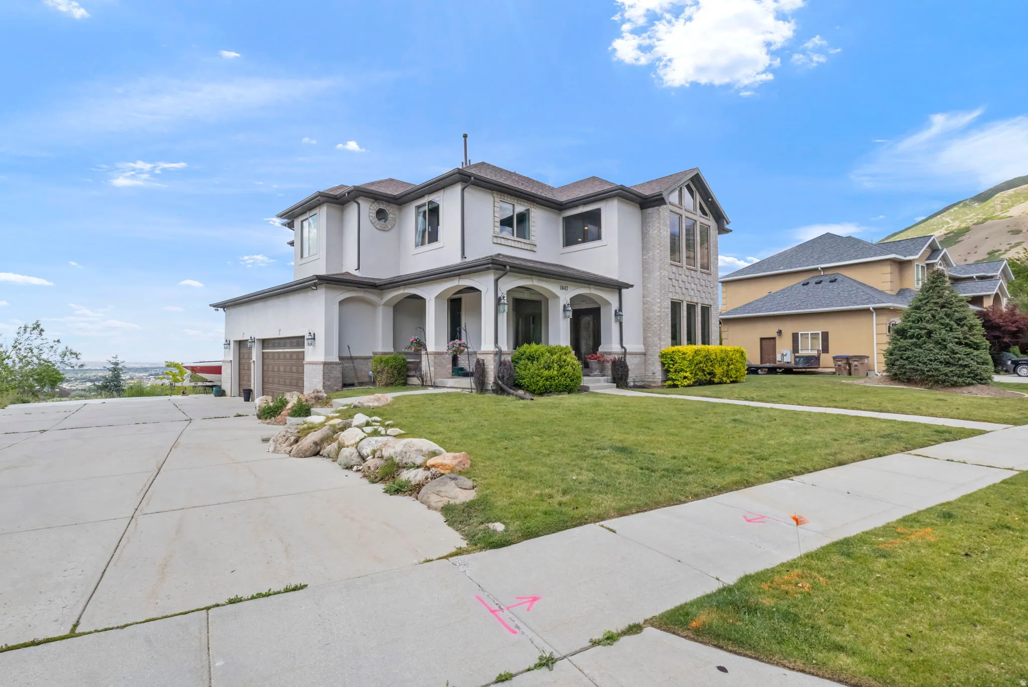 Stucco and stone exterior residence featuring a multi-car garage, covered entry, front lawn, and concrete driveway