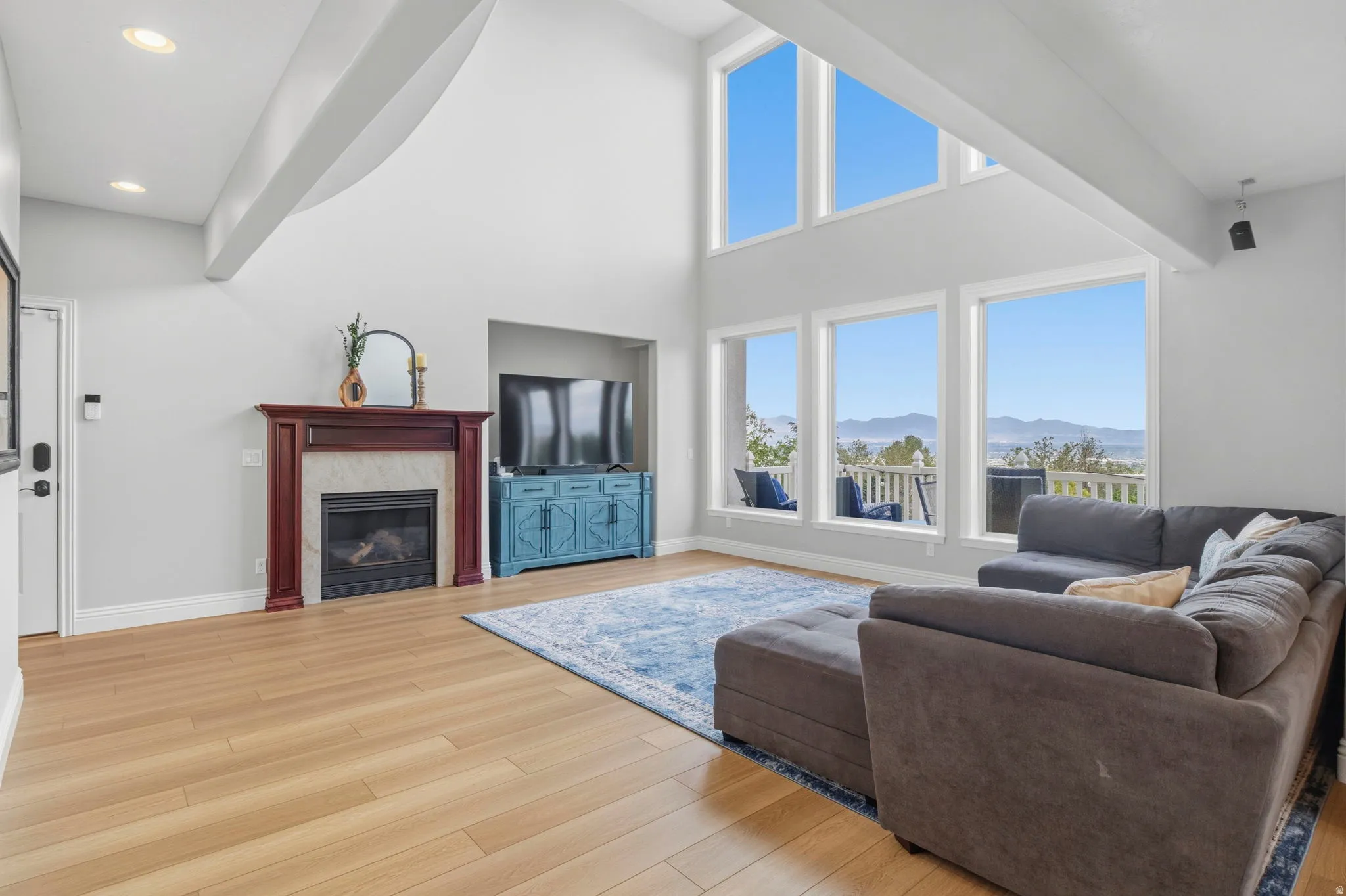 Vaulted ceilings define this living space, featuring a fireplace with a wood-finish mantel, wood-finish flooring, and expansive windows offering mountain scenery