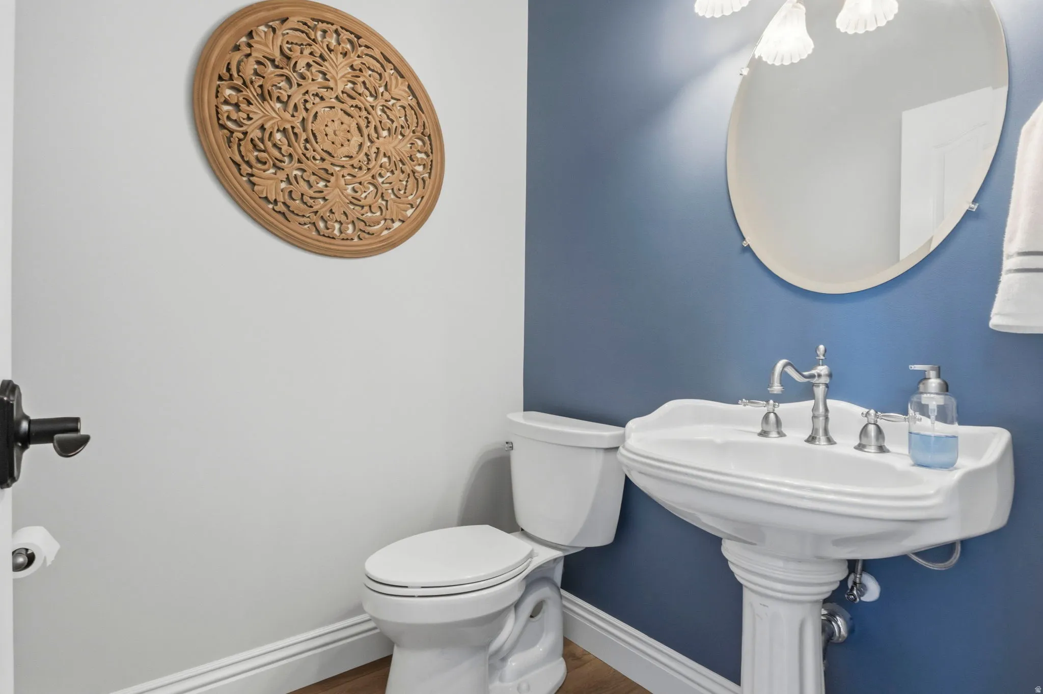 Pedestal sink with satin nickel faucet set, oval mirror, and three-light vanity fixture