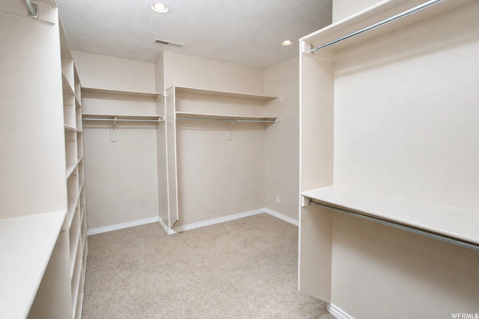 Primary Closet. Spacious walk-in closet featuring extensive built-in shelving, multiple hanging rods, recessed ceiling lighting, and neutral carpeting