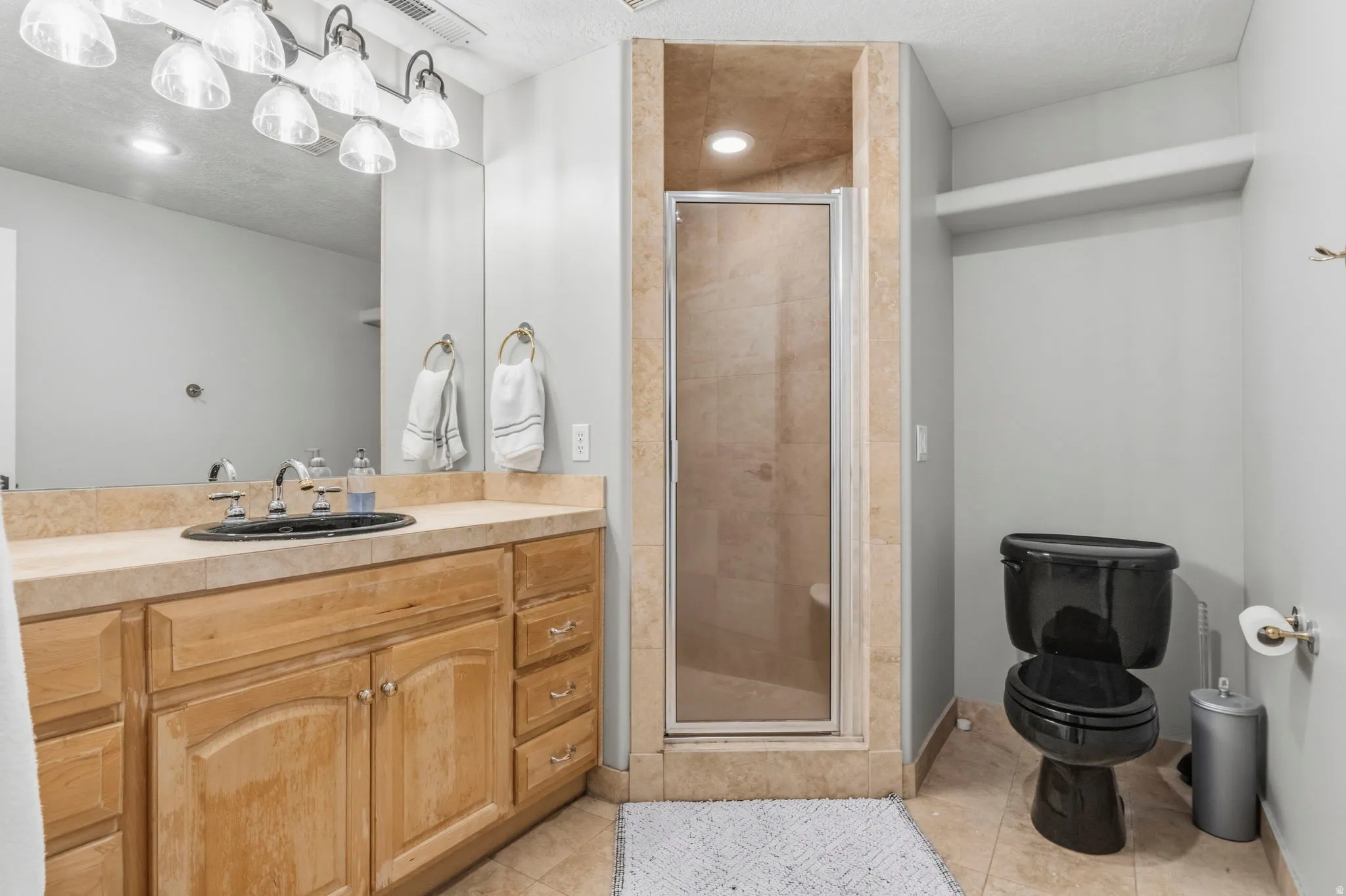 Bathroom featuring a light wood vanity with a black drop-in sink, a large mirror, and a multi-bulb vanity light fixture