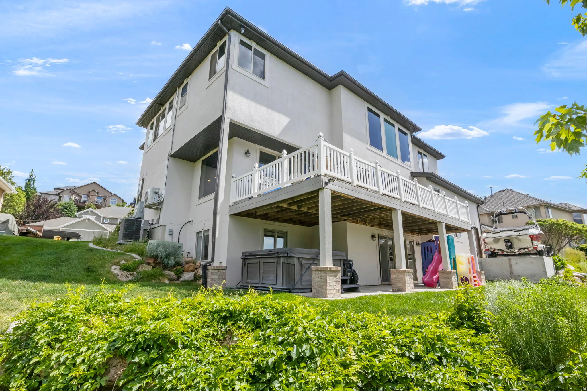Multi-level stucco exterior featuring a spacious upper deck with white railing and a covered patio below