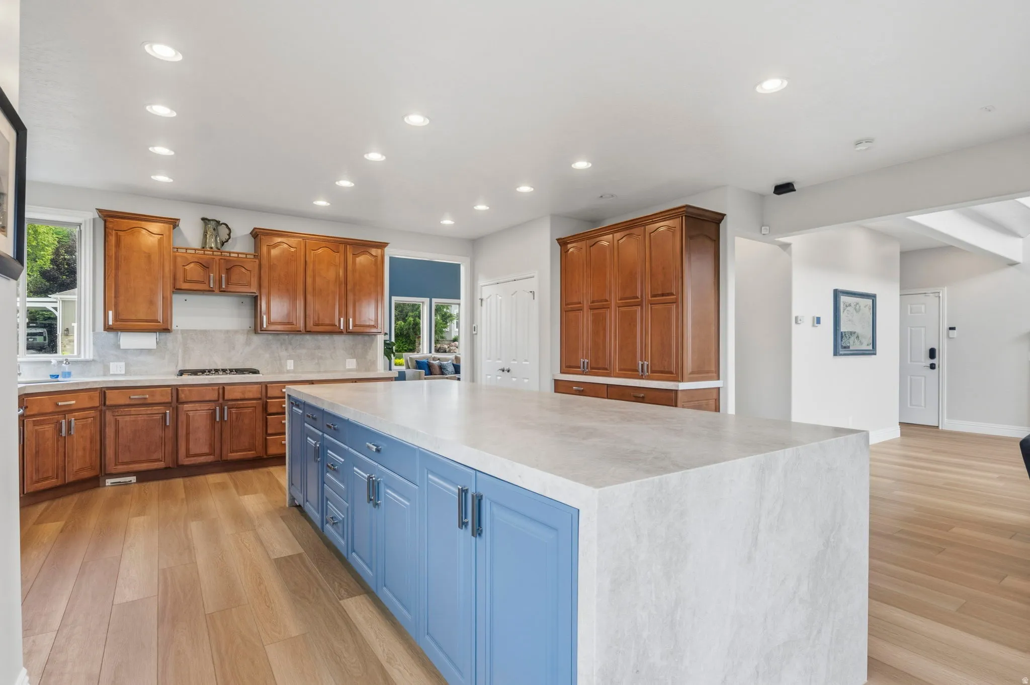 Spacious kitchen featuring a large central island with blue cabinetry, light-toned countertops, wood-finish flooring, and recessed lighting