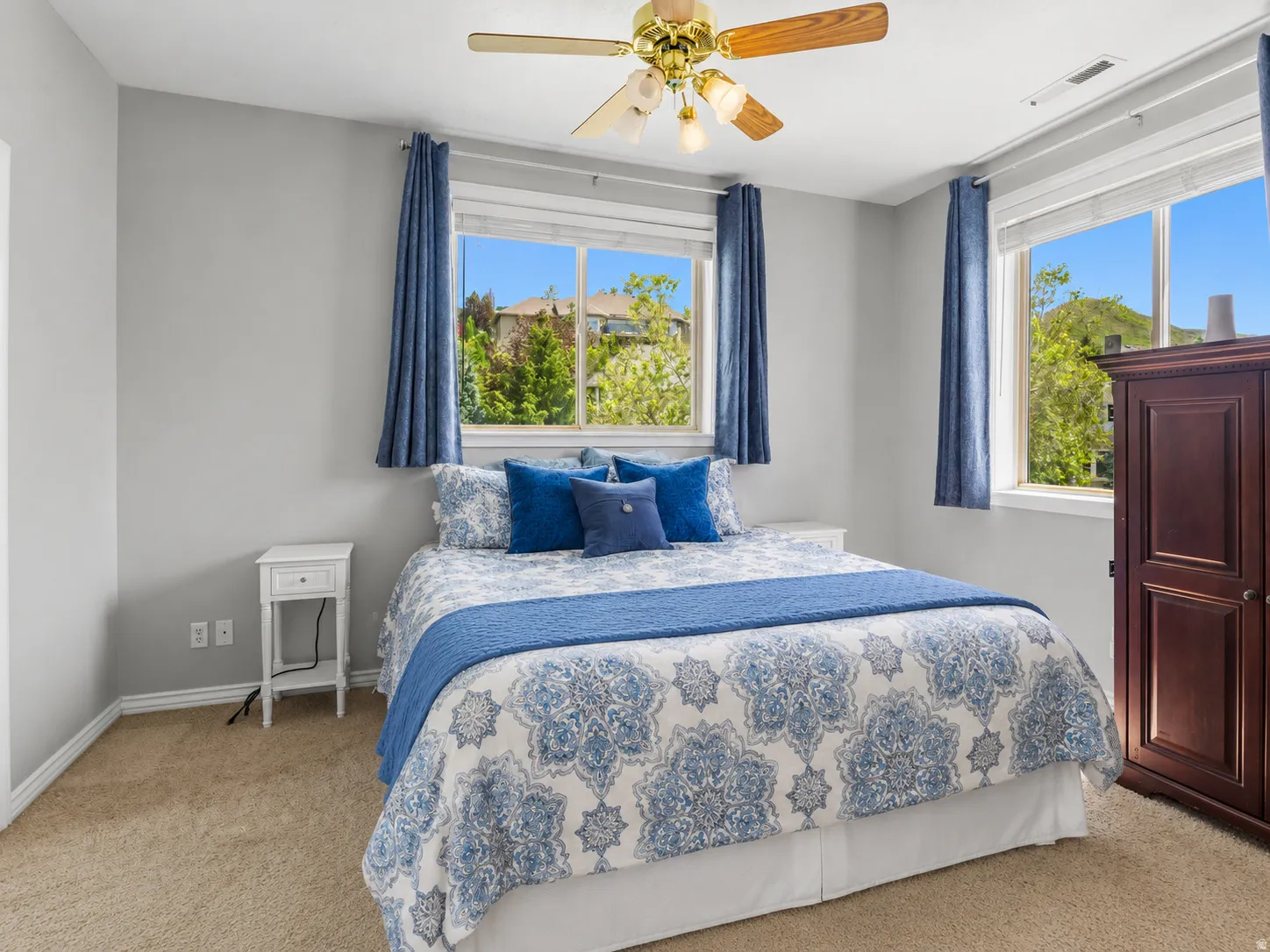 Bedroom featuring two windows, neutral carpet, and a brass-finish ceiling fan with wood-tone blades
