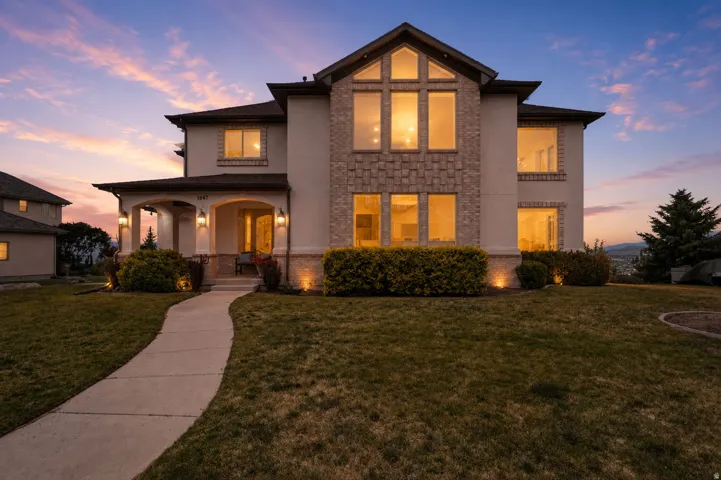 Stucco and stone facade home featuring a covered entry, extensive front windows including a two-story arched window, and a concrete curved pathway with a beautiful valley view