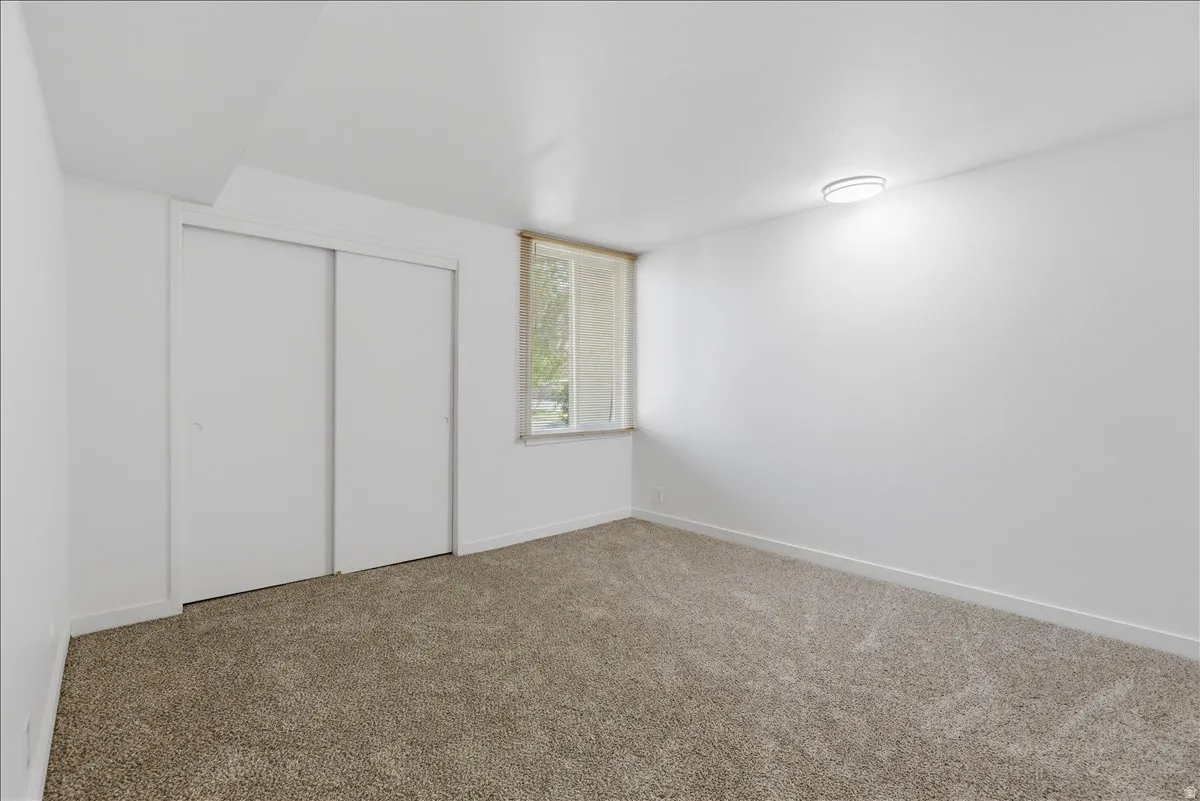 Room featuring light brown carpet, white walls, and a window with horizontal blinds