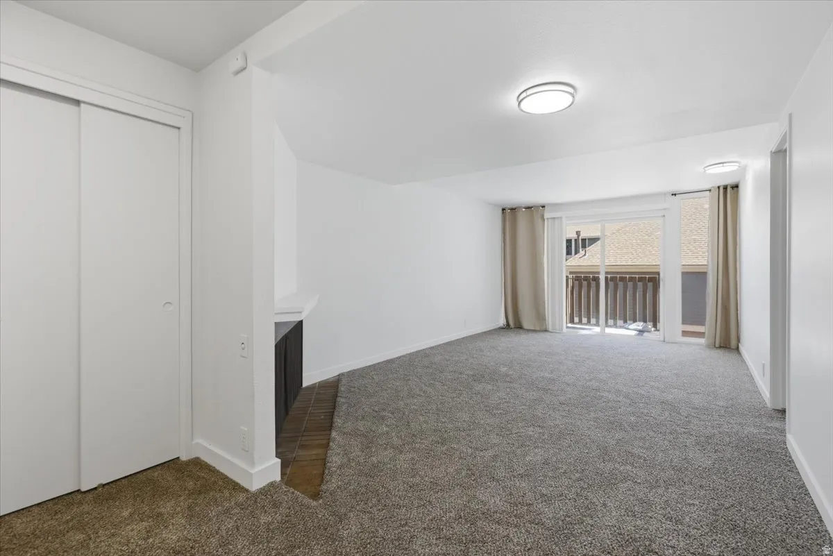 Carpeted living area featuring a built-in fireplace, sliding glass door to a balcony, and two recessed ceiling light fixtures
