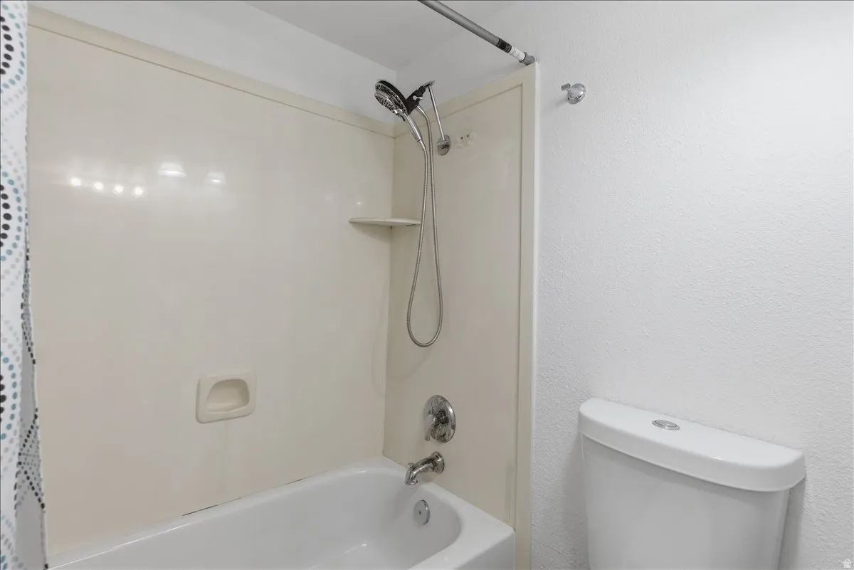 White bathtub with integrated shower, white wall surround, and chrome fixtures