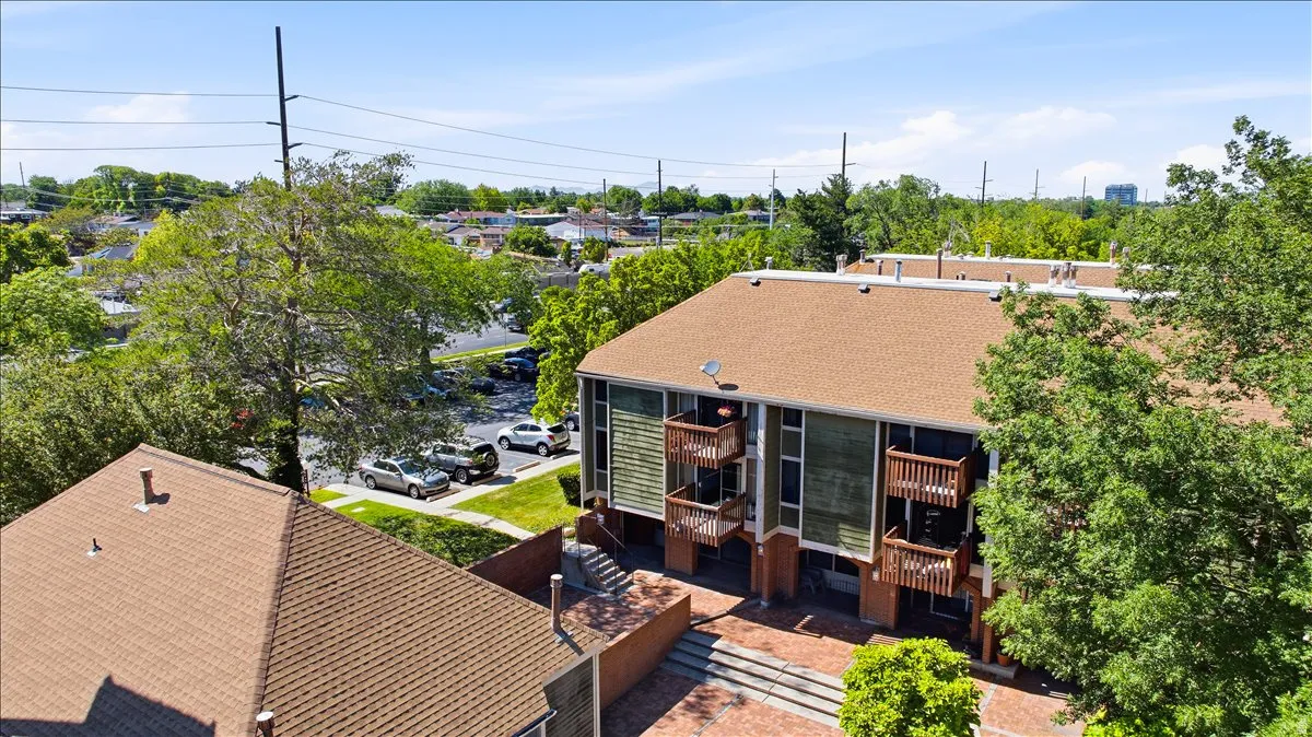 Multi-level residential building featuring private balconies with wood railings, a brown shingle roof, and a red brick patio area