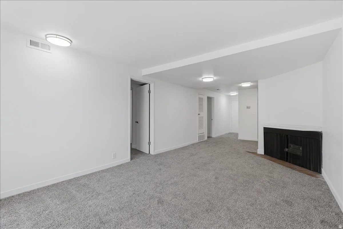 Spacious room featuring light gray carpeting, crisp white walls, recessed lighting, and a dark-toned fireplace with a mantel