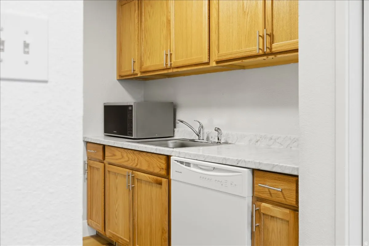 Kitchenette featuring wood cabinetry, laminate countertops, stainless steel sink with chrome faucet, and white dishwasher