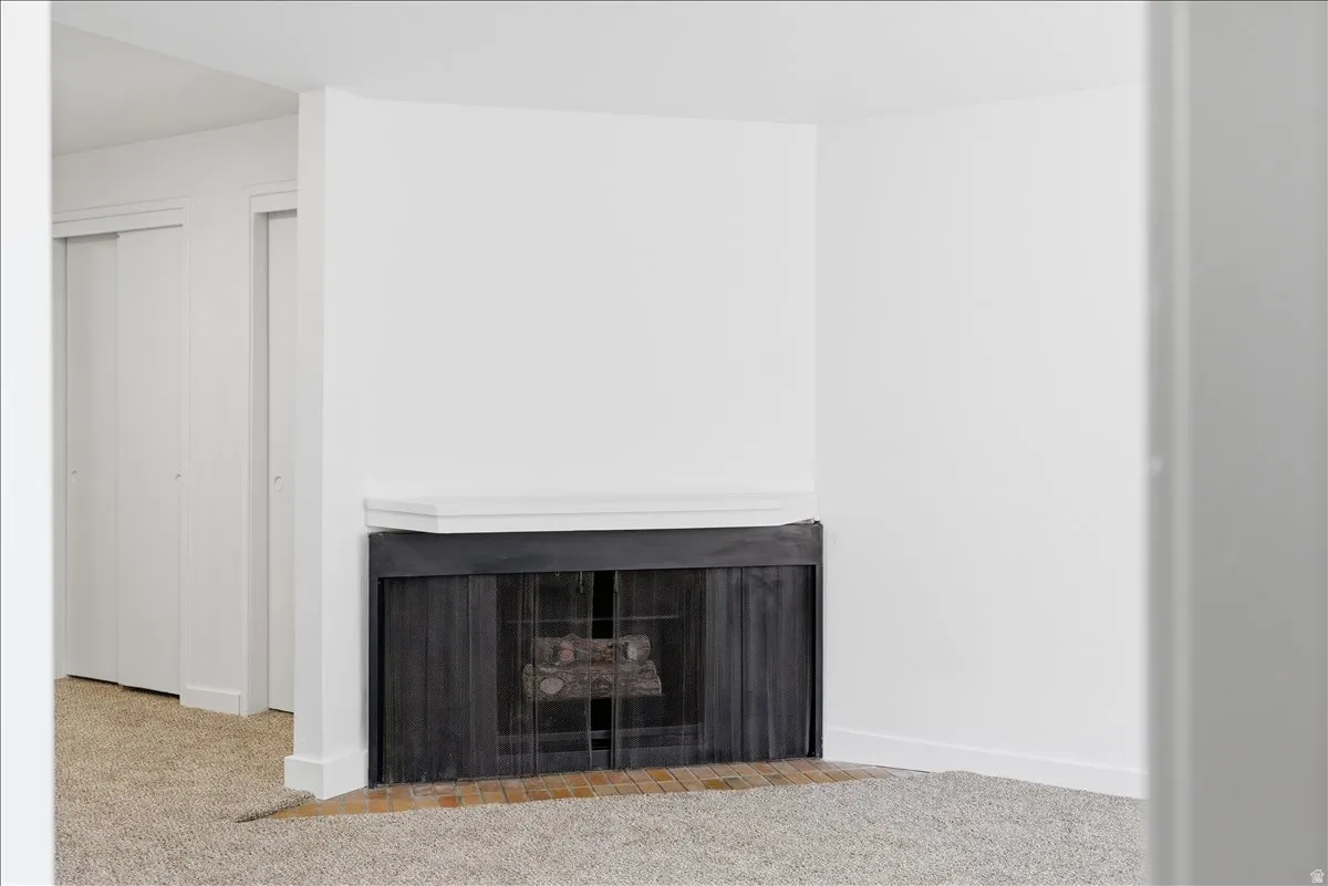 Corner fireplace with a white mantel, black metal screen, and a brick hearth
