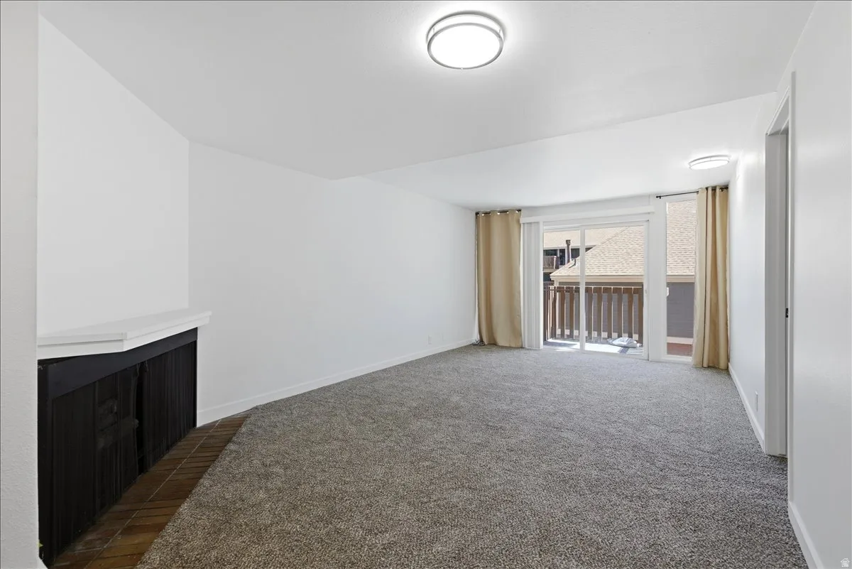 Spacious room featuring new carpeting, a corner fireplace with a white mantel, and a sliding glass door providing exterior access