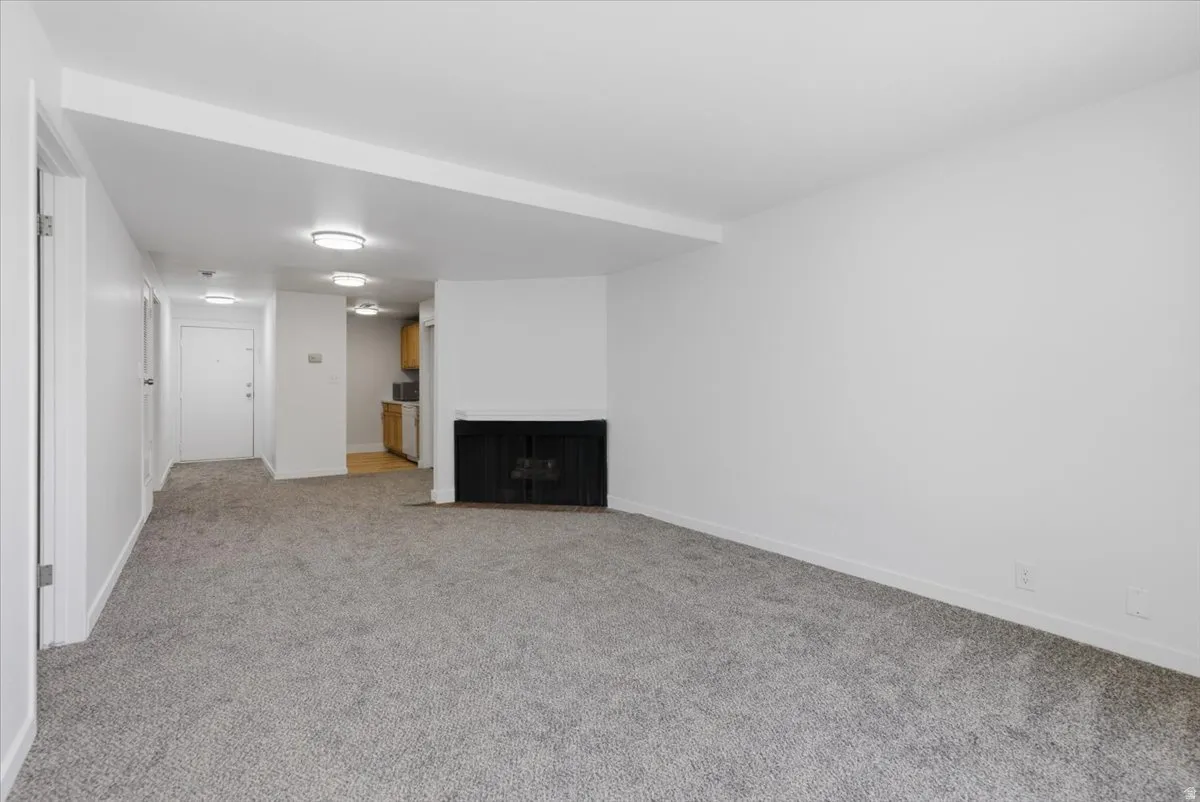 Spacious living area featuring new gray carpet, a built-in black fireplace, white walls, and flush-mount ceiling lighting