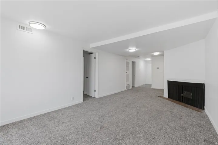 Spacious room featuring light gray carpeting, crisp white walls, recessed lighting, and a dark-toned fireplace with a mantel