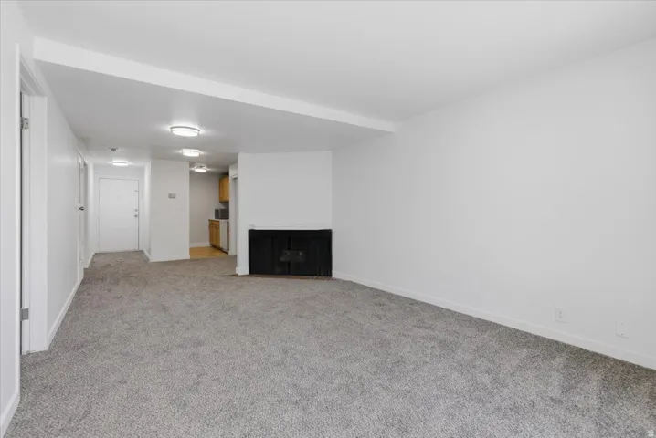 Spacious living area featuring new gray carpet, a built-in black fireplace, white walls, and flush-mount ceiling lighting