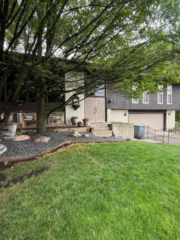 Split-level residence featuring a prominent front entrance with double doors, a two-car garage, and a lush front lawn with mature trees