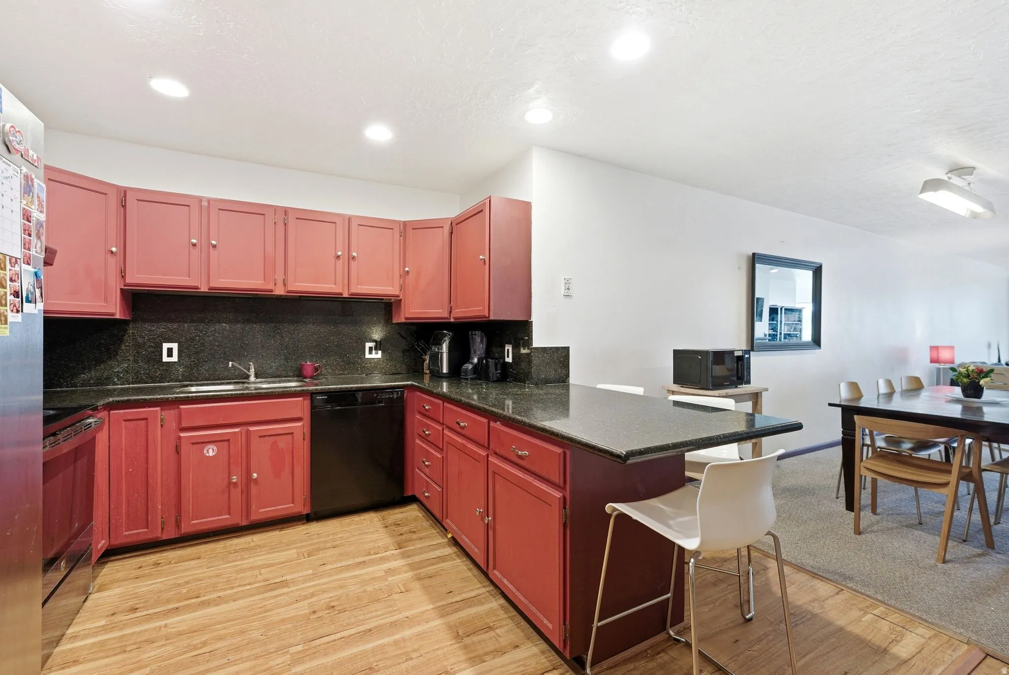 Kitchen featuring red cabinetry, dark countertops, wood-finish flooring, recessed lighting, and a built-in dishwasher