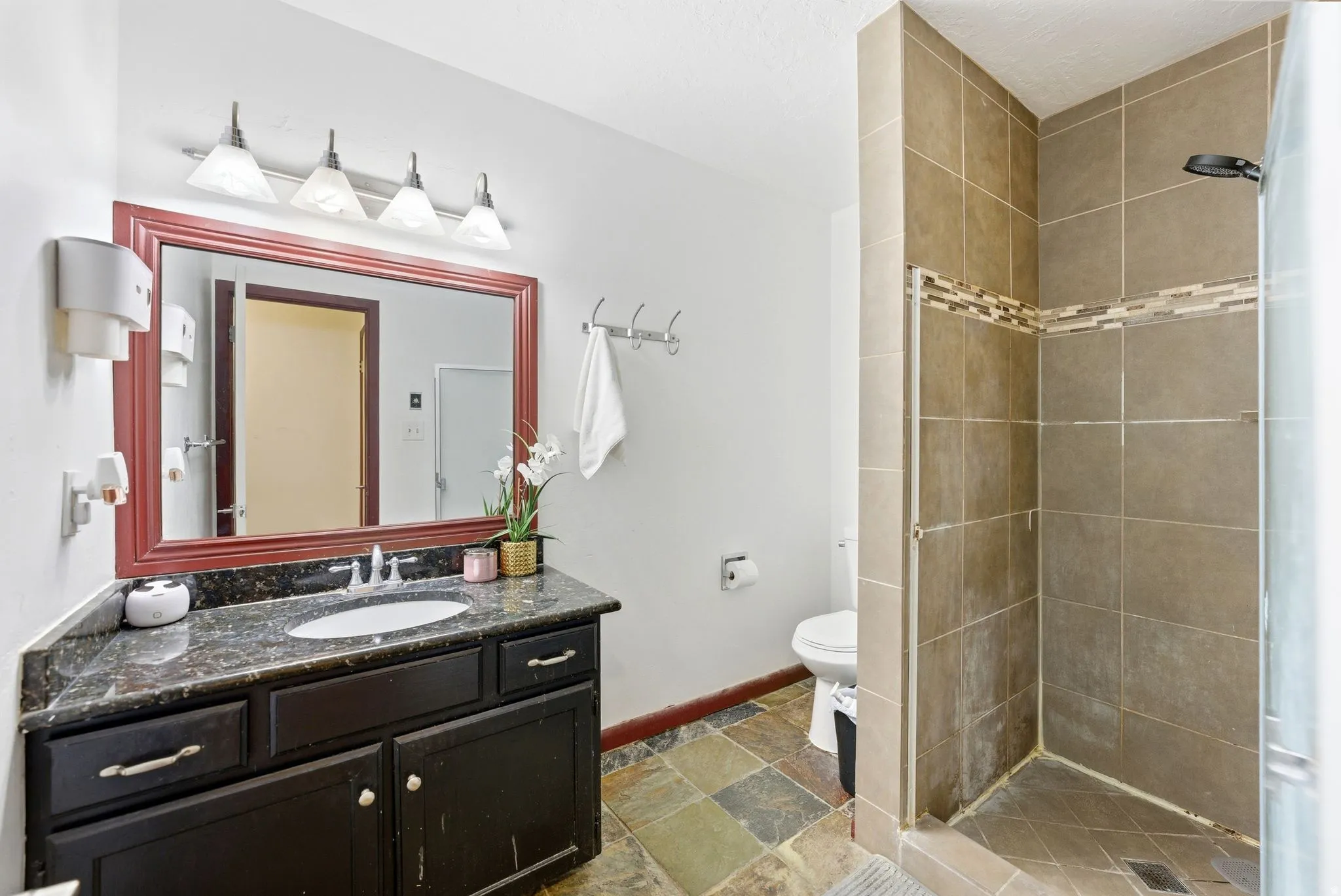 Bathroom featuring a dark wood vanity with a stone countertop, a framed mirror, and a walk-in shower with tile surround and decorative accent band
