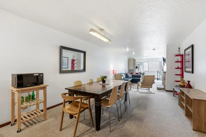 Open-concept living space featuring a dining area with a dark wood table, neutral carpeting, and white walls throughout
