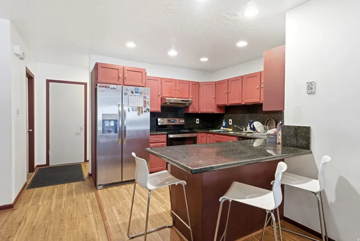 Kitchen featuring wood-finish flooring, recessed lighting, stainless steel appliances, dark stone countertops, and a peninsula with seating