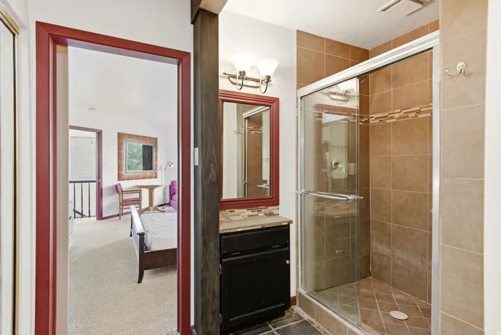 Full bathroom featuring a glass-enclosed shower with tile surround and decorative accent band, dark wood vanity with a stone countertop, and a red-framed mirror with wall-mounted lighting