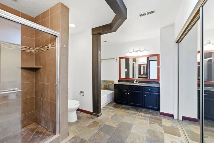 Spacious bathroom featuring a glass-enclosed shower with tile surround and integrated shelf, a vanity with dark cabinetry and countertop, a large framed mirror, and slate-finish floor tiles
