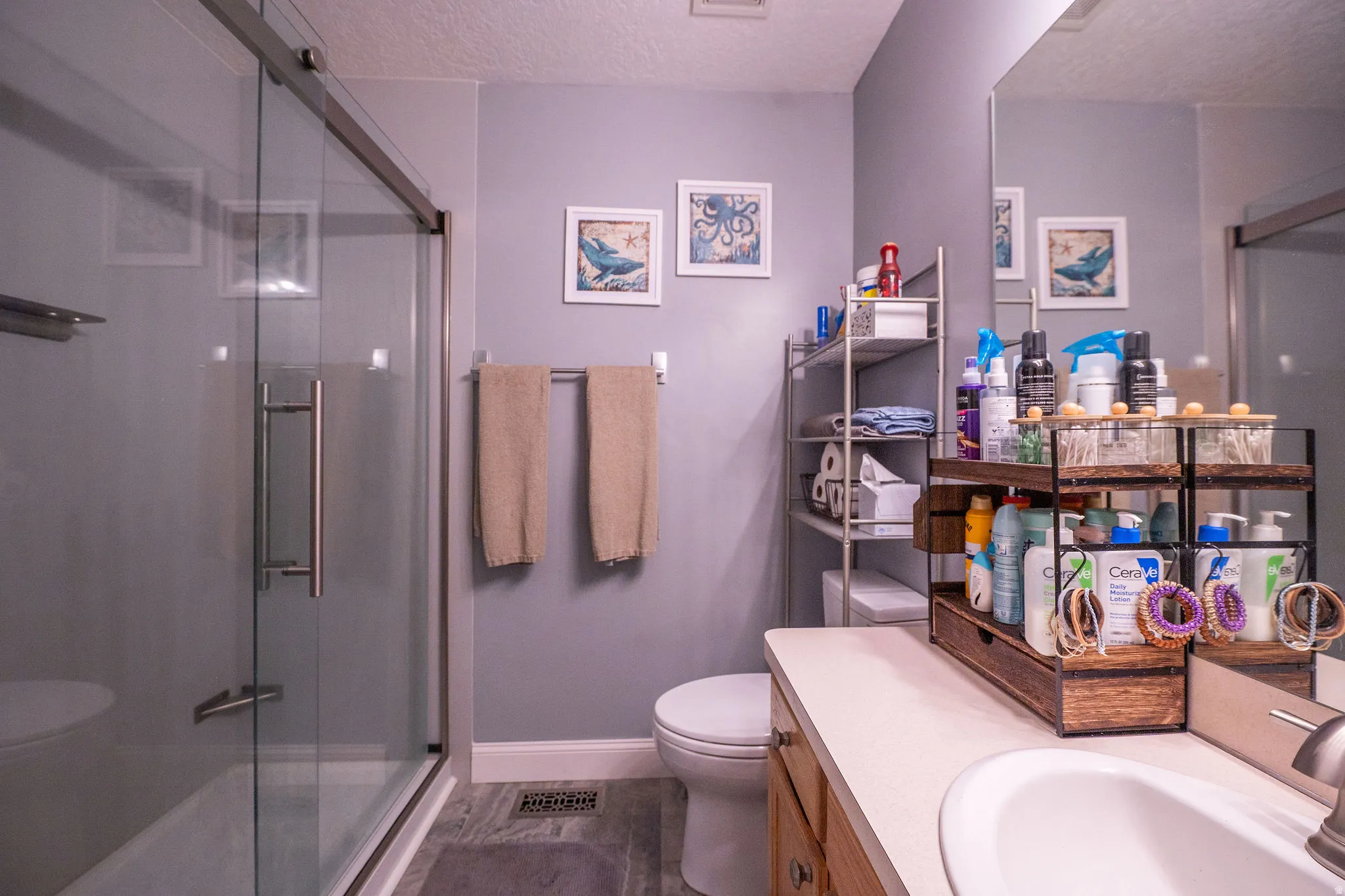 Bathroom featuring a glass-enclosed shower, wood-finish vanity with an integrated sink, broad wall mirror, and grey-toned flooring
