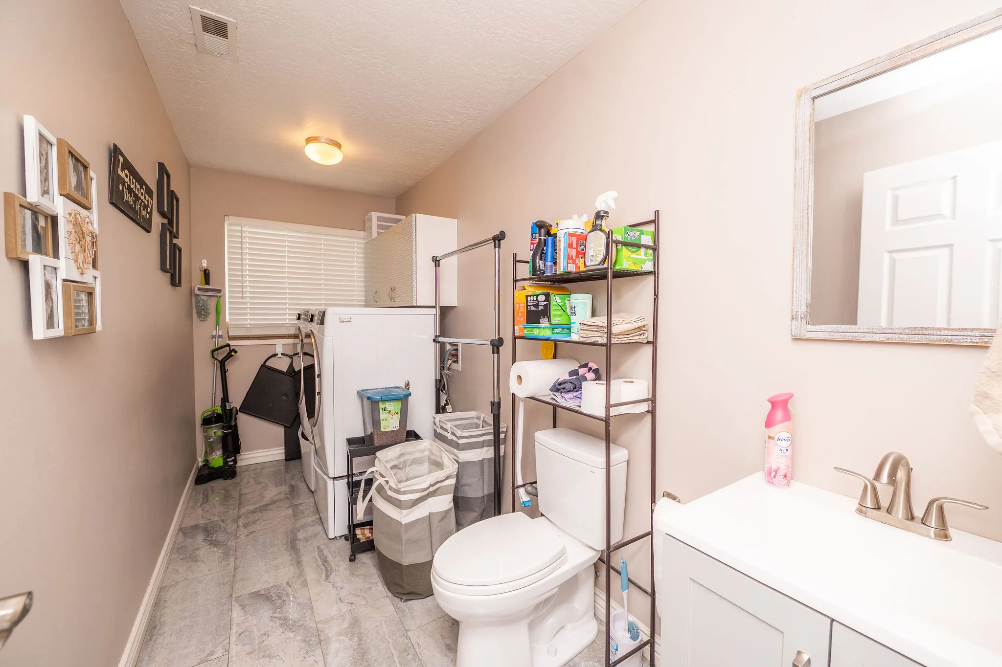 Combined laundry and bathroom space featuring gray-toned flooring, a window with blinds, and white appliances