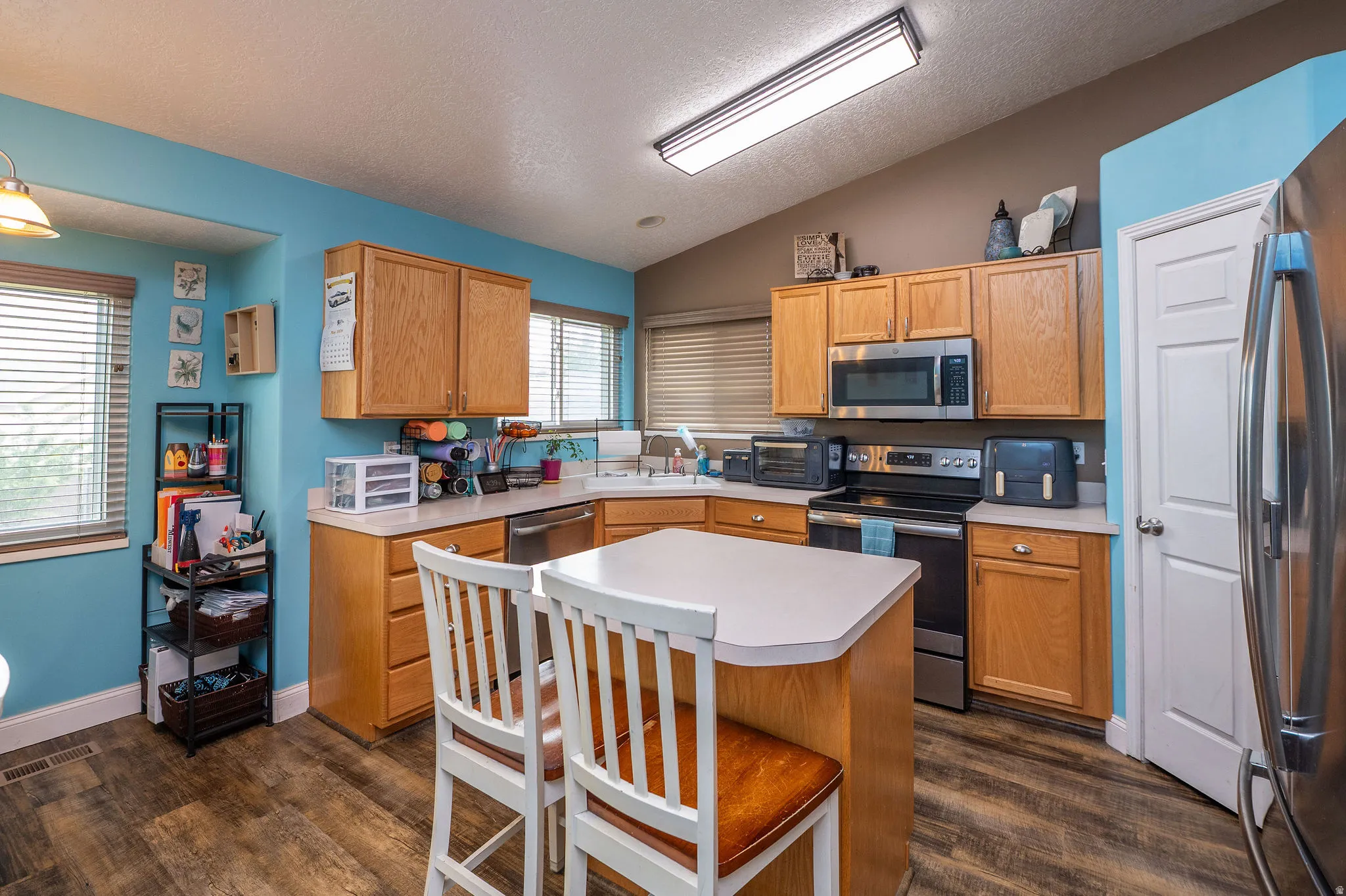 Kitchen featuring a central island, wood-finish flooring, light wood cabinetry, stainless steel appliances, and a vaulted ceiling