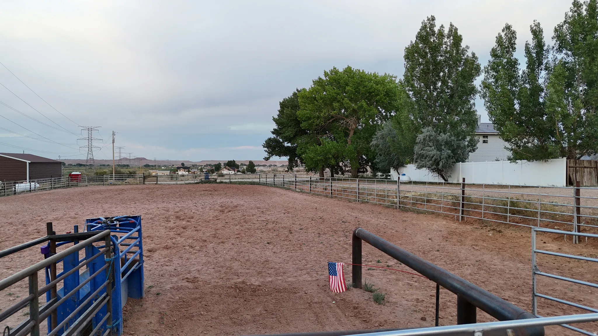 Spacious outdoor arena featuring a dirt surface, perimeter fencing, and mature trees