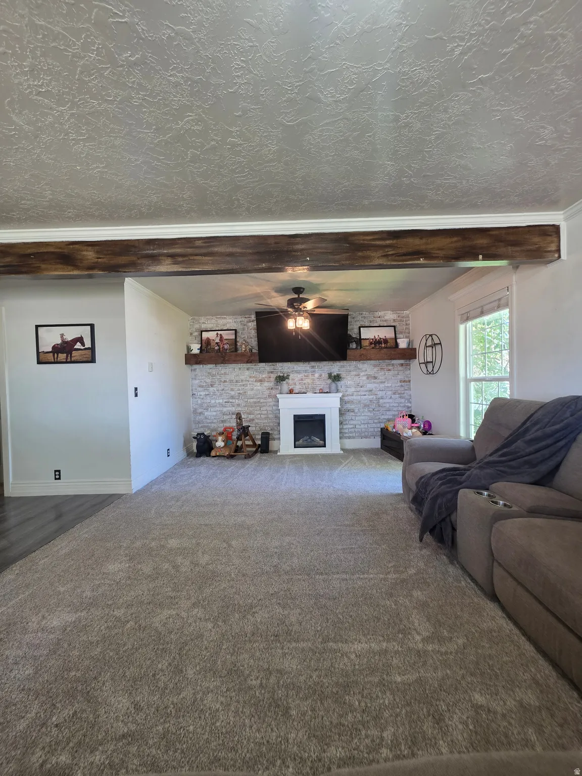 Living area with a textured ceiling, a decorative wood-finish beam, and carpet flooring