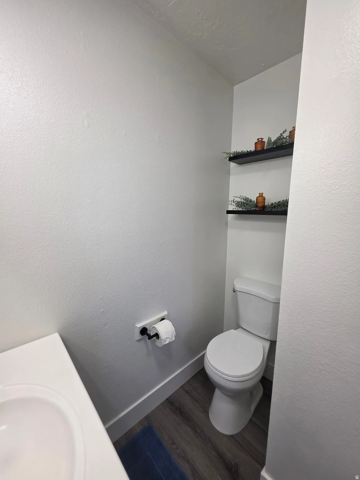 Compact powder room featuring a white toilet, integrated sink vanity, and wood-finish flooring