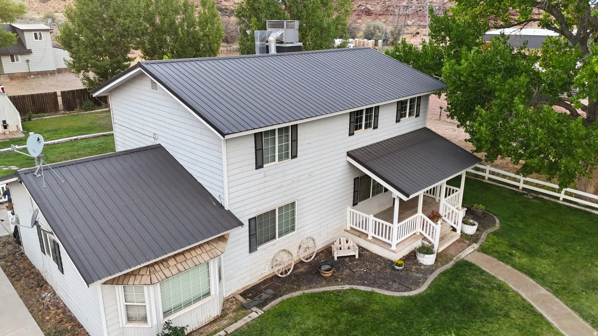Two-story residence featuring a dark metal roof, light-colored siding, and a covered front porch with white railings