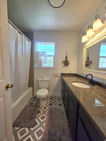 Bathroom featuring a dark wood-finish vanity with a stone countertop, a single basin sink, and a matte black faucet