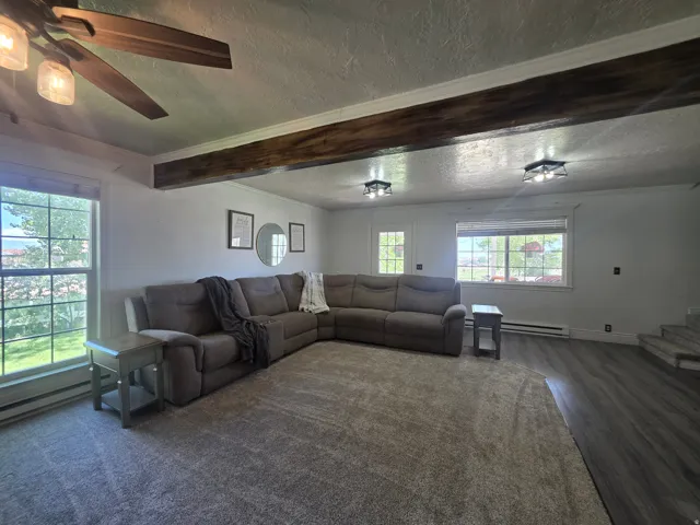 Spacious living area featuring exposed wood-finish beam, wood-finish ceiling fan, wood-finish flooring, recessed lighting fixtures, and light-toned carpeting