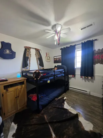 Room featuring wood-finish flooring, a window with dark drapes, and a white ceiling with a ceiling fan