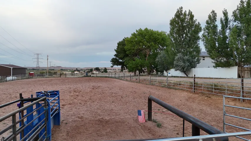 Spacious outdoor arena featuring a dirt surface, perimeter fencing, and mature trees