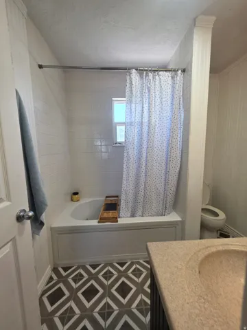 Bathroom featuring a combination shower and tub with white tile surround, a window, and patterned geometric floor tiles