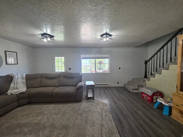 Spacious living area featuring contemporary wood-finish flooring, a carpeted section, and a staircase with dark balusters and handrail