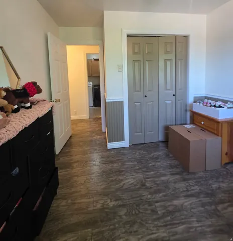 Interior room featuring wood-finish flooring, bi-fold closet doors, white trim, and wainscoting details