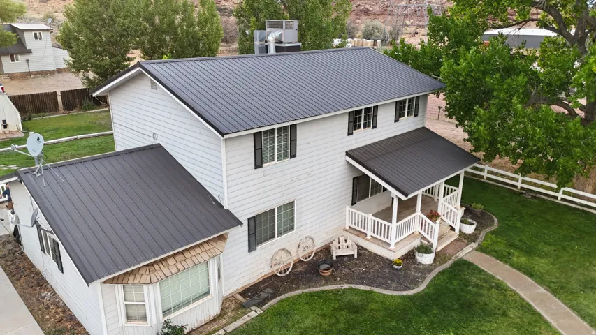 Two-story residence featuring a dark metal roof, light-colored siding, and a covered front porch with white railings