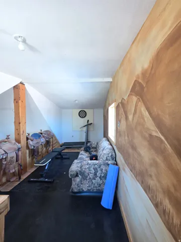 Spacious room featuring a decorative mural wall, exposed wood beam, recessed wall paneling, and durable black flooring