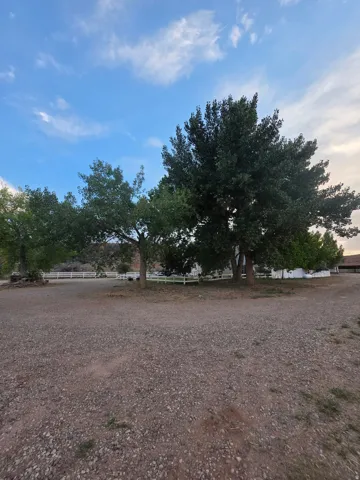 Expansive gravel area with mature trees and a white perimeter fence