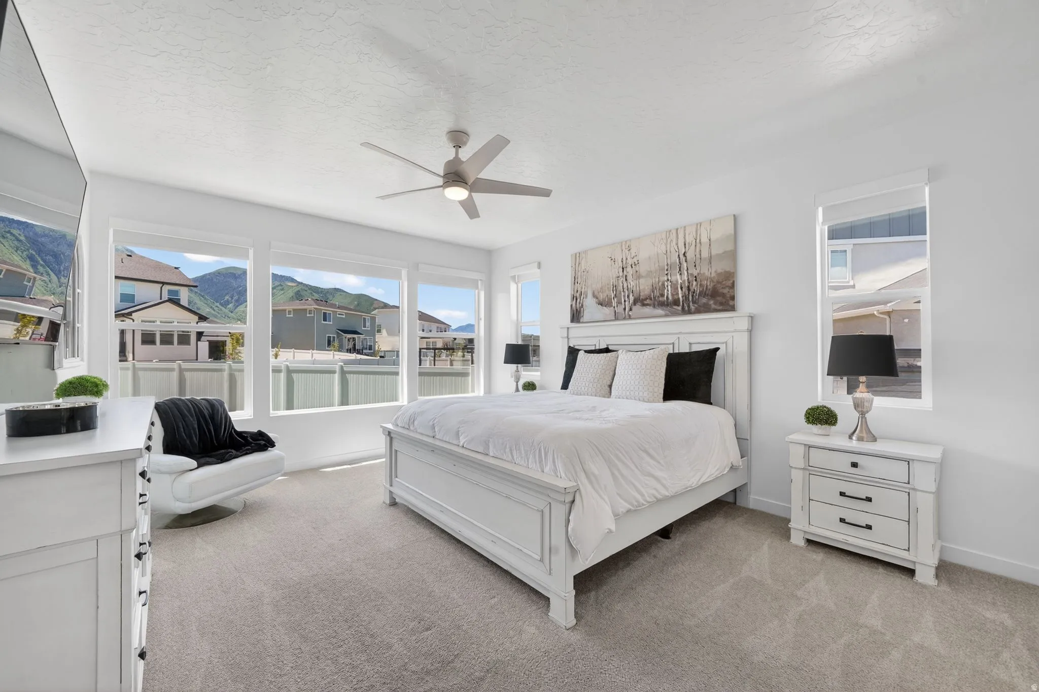 Spacious room featuring multiple large windows, light gray patterned carpeting, a modern ceiling fan, and white walls